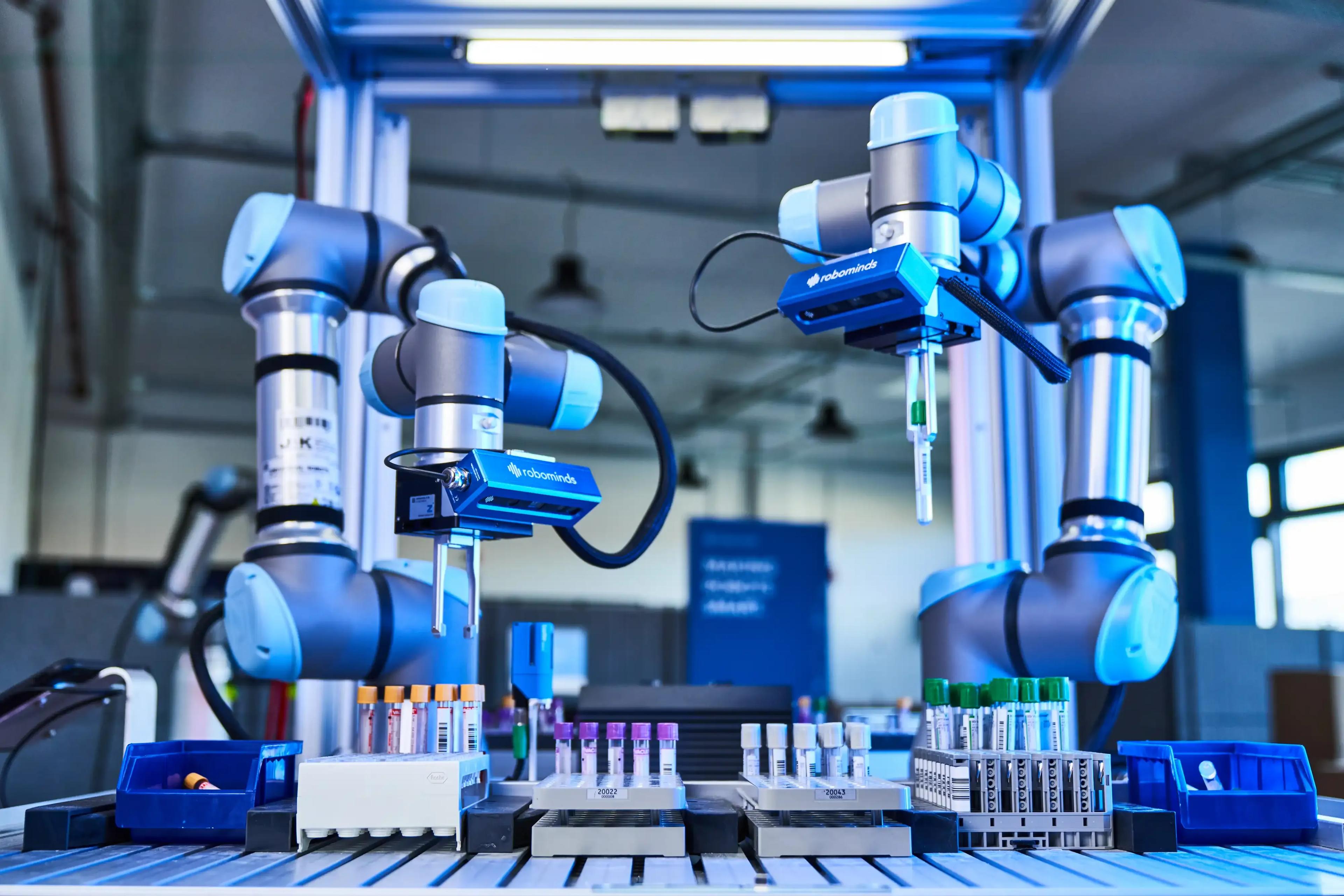 Two robotic arms equipped with advanced AI technology are identifying, sorting, and placing laboratory sample tubes into racks, demonstrating automated sample handling in a modern lab setting.