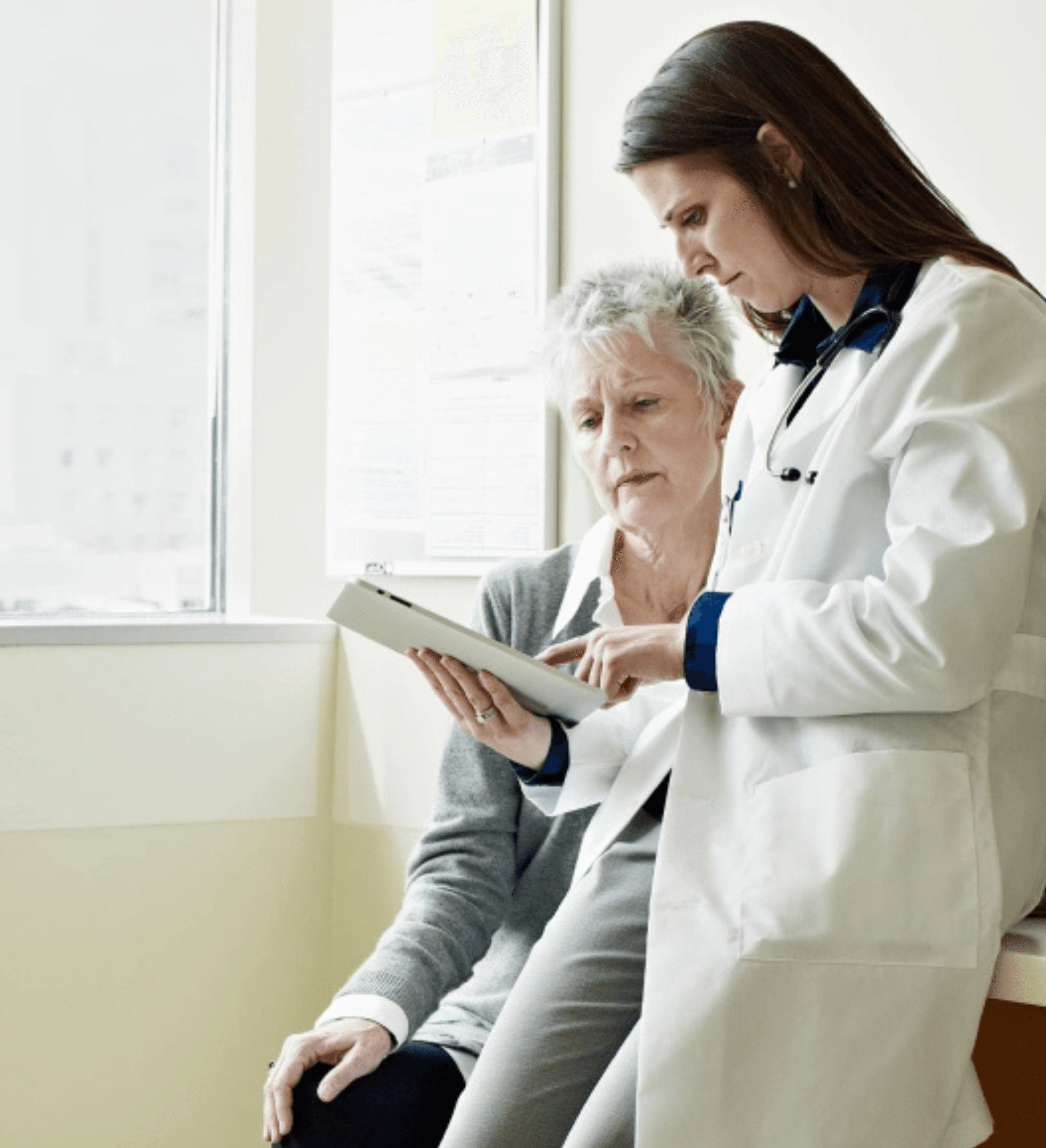 A doctor in a white coat shows an elderly patient details on a tablet.