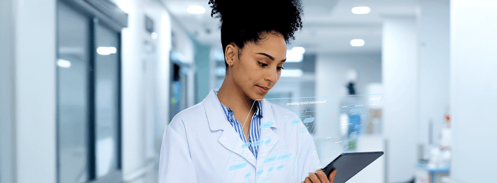 A healthcare professional in a lab coat examines data on a transparent digital screen in a bright hallway.
