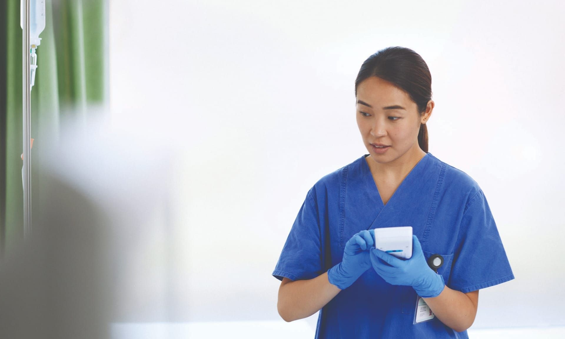 A female healthcare professional wearing protective gloves and holding a white device.