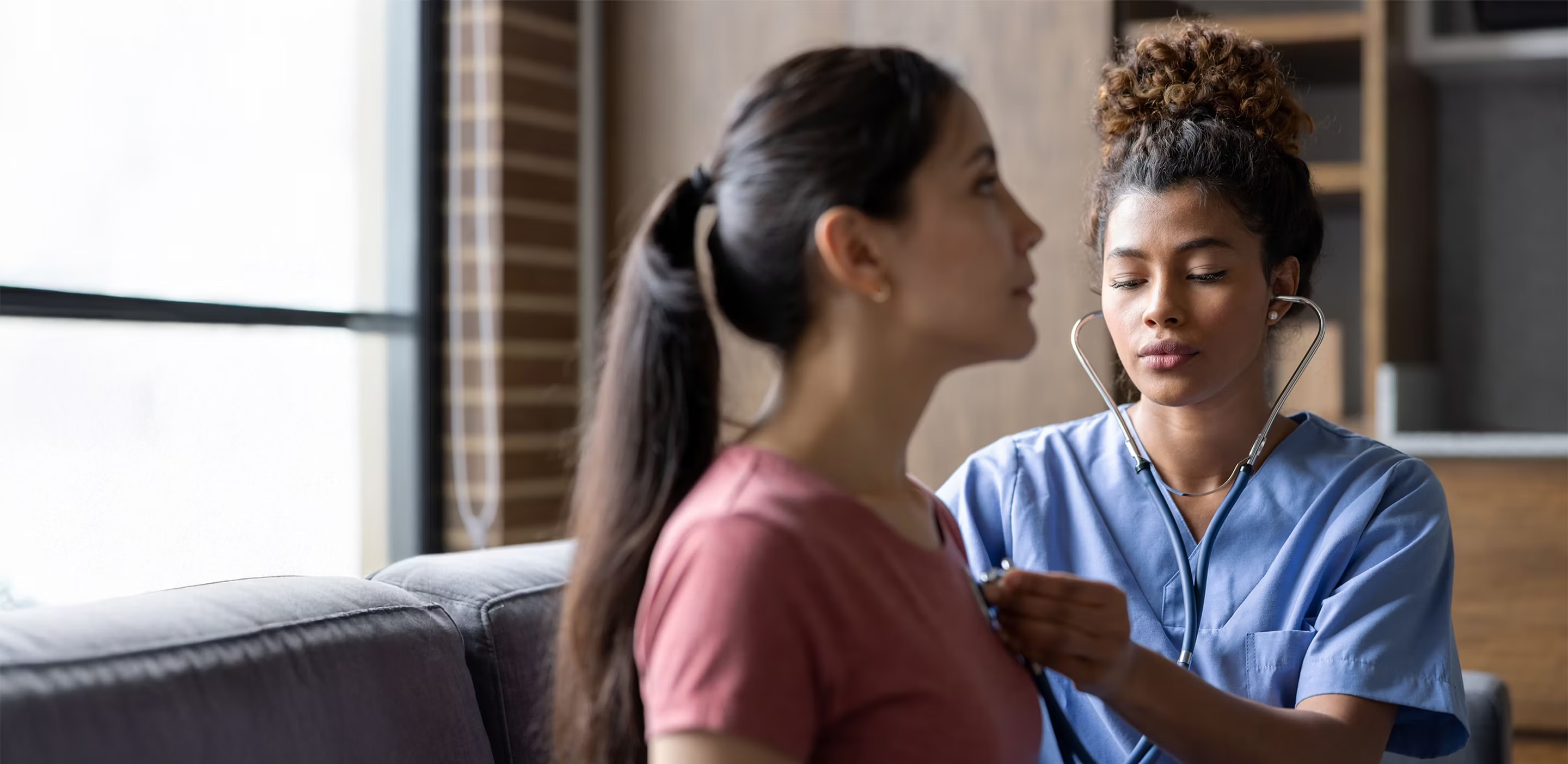 Healthcare professional using a stethoscope to listen to a patient's chest during a medical examination in a clinical setting.