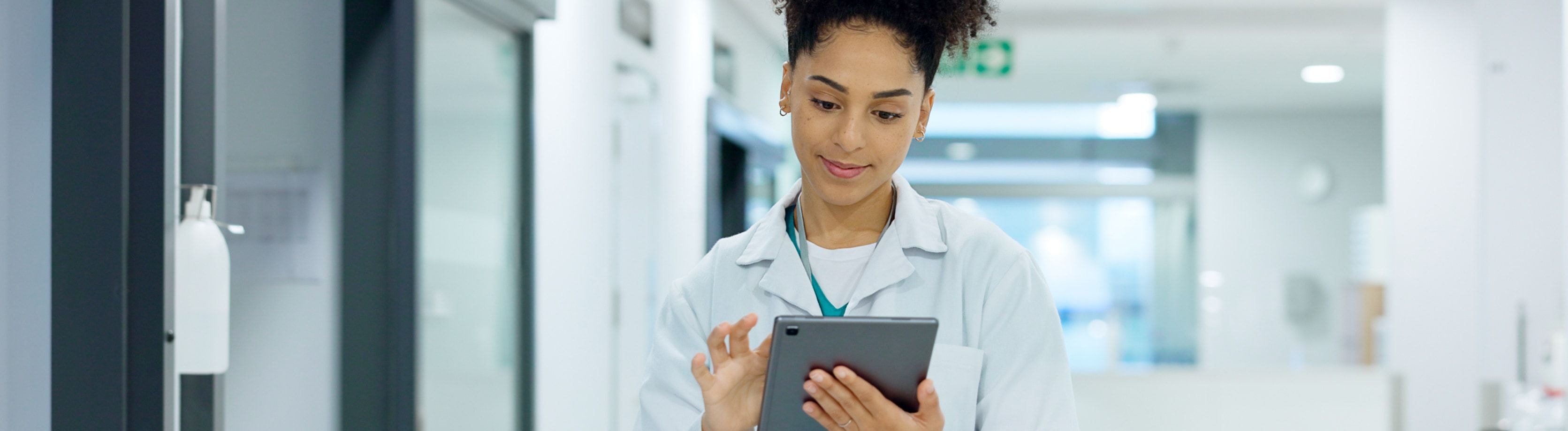 A healthcare professional using a tablet in a hospital corridor, focused on managing lab operations through a digital interface.