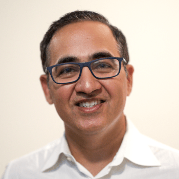 A portrait of Dr. Navdeep Tangri smiling, wearing glasses and a white collared shirt.