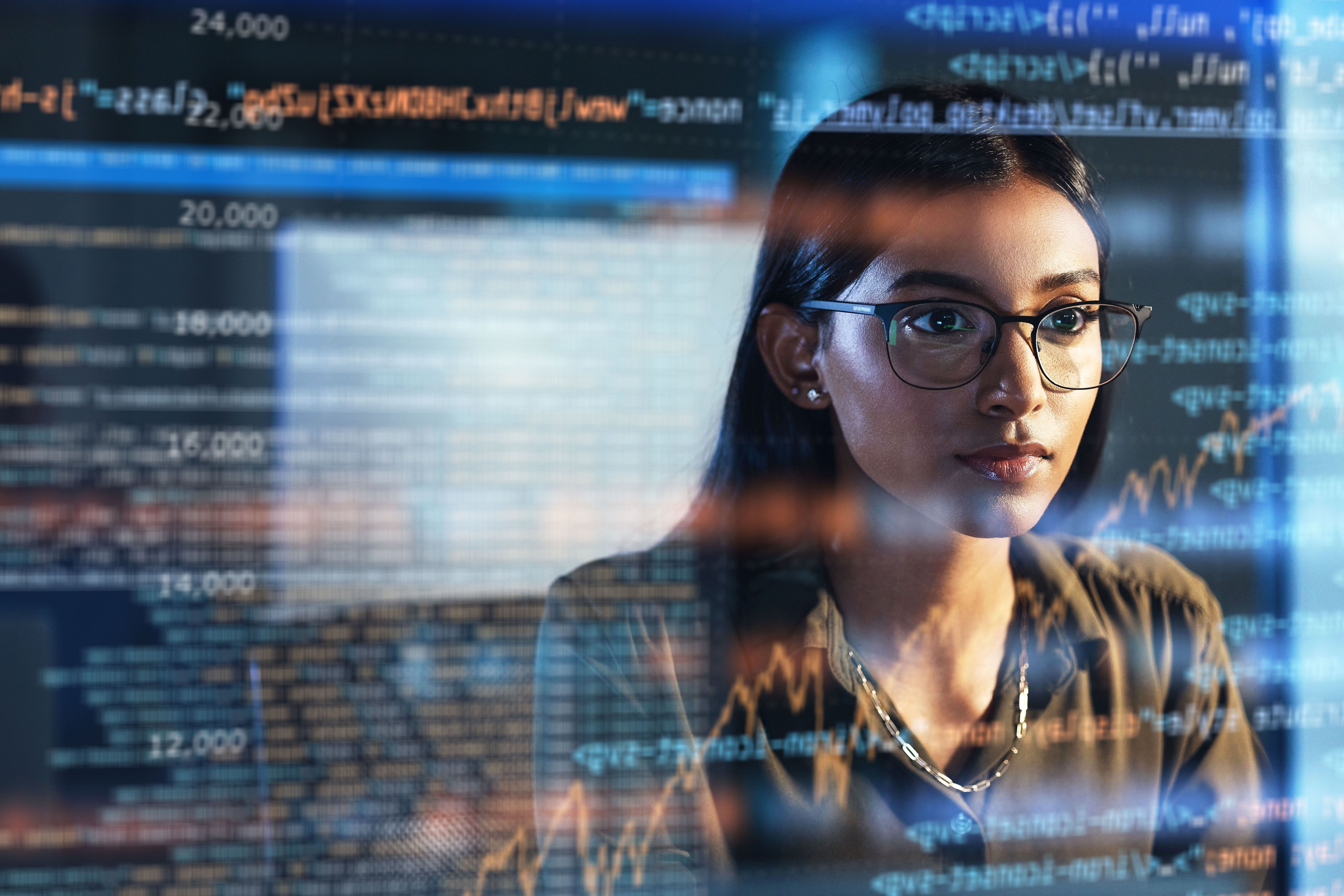Male IT specialist focused on coding or system monitoring, working in a modern office with multiple monitors displaying data.