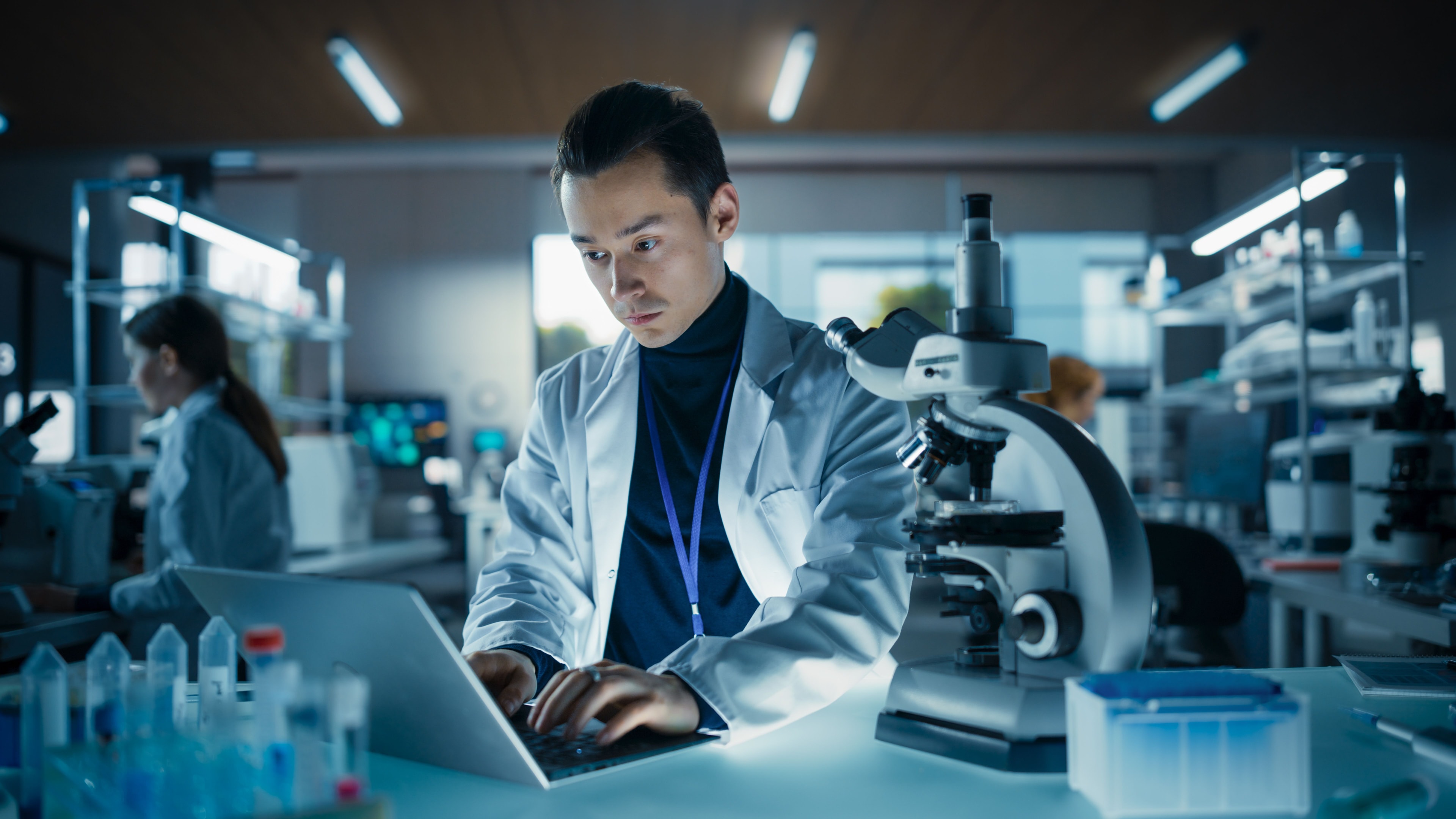 Laboratory scientist using laptop to review data, ensuring quality control in a medical lab environment.