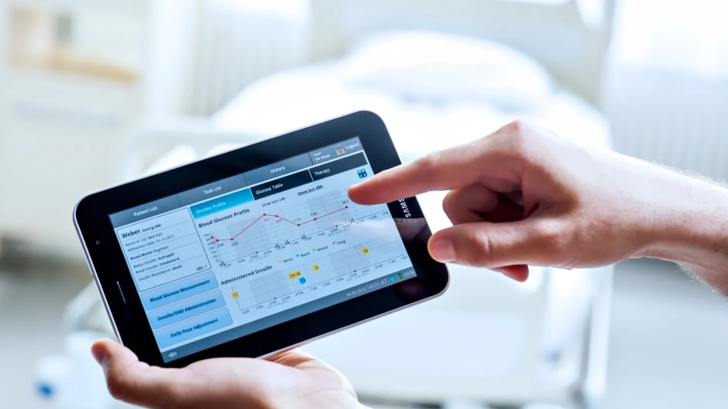A healthcare professional using a tablet to monitor and adjust insulin therapy for a hospitalized diabetes patient through the GlucoTab® system.