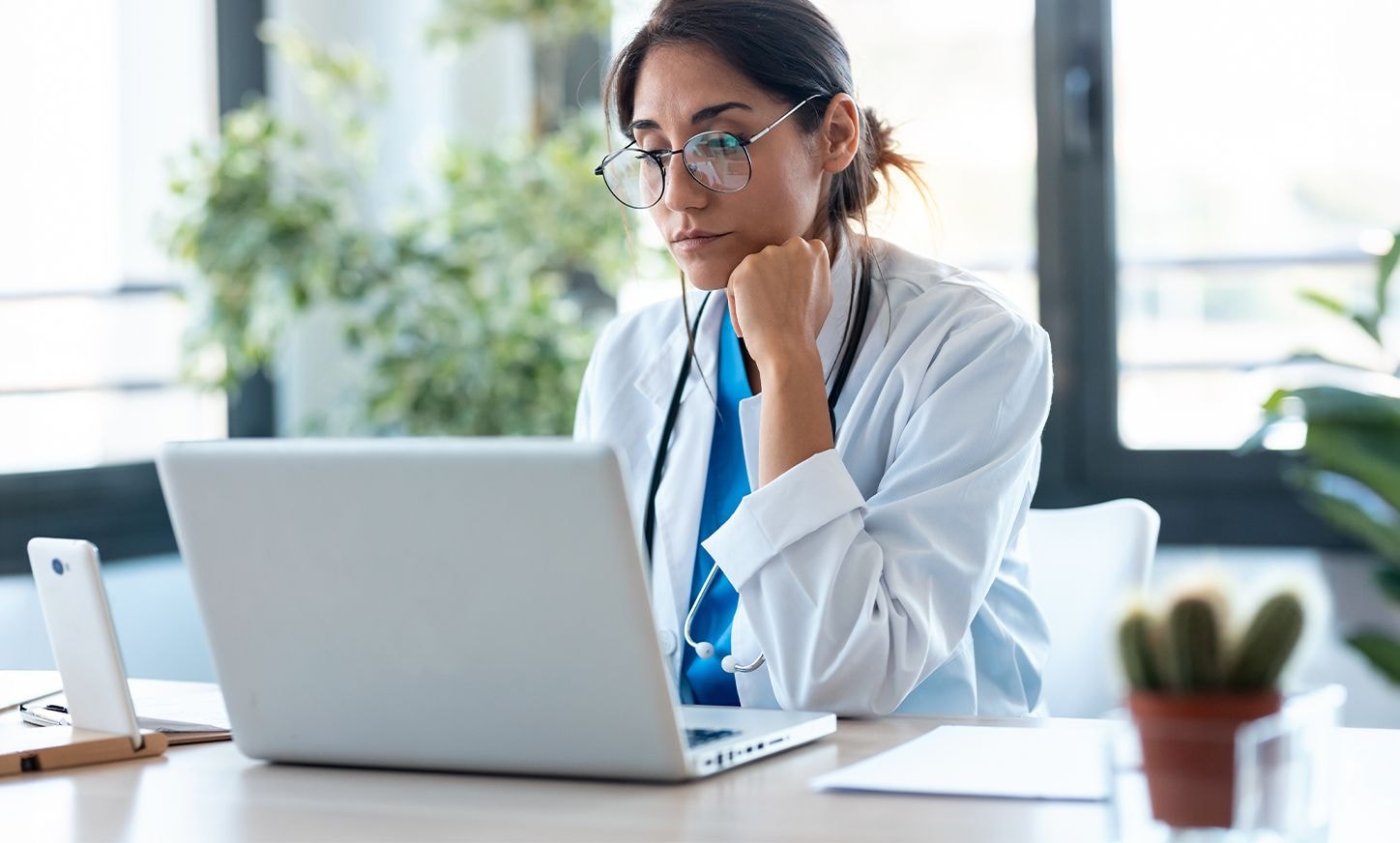 Healthcare professional reviewing medical data on laptop in modern clinical office environment.