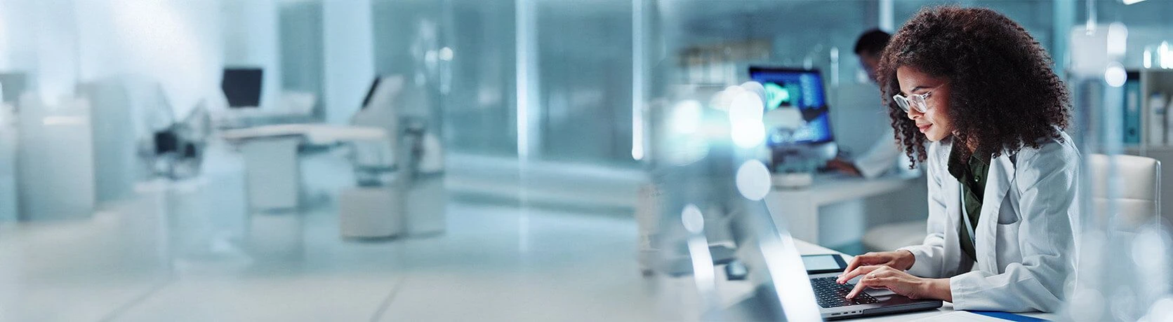 Female scientist in a lab coat working by a computer in a lab environment.