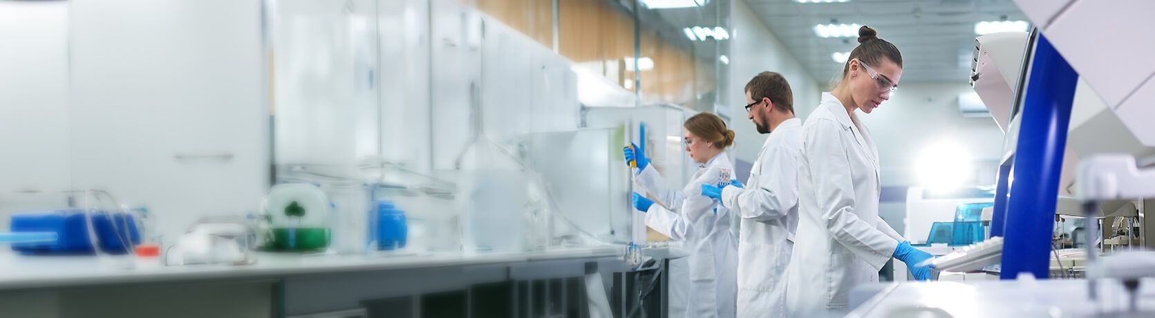 Lab technicians in a laboratory with lab equipment and supplies in the background.