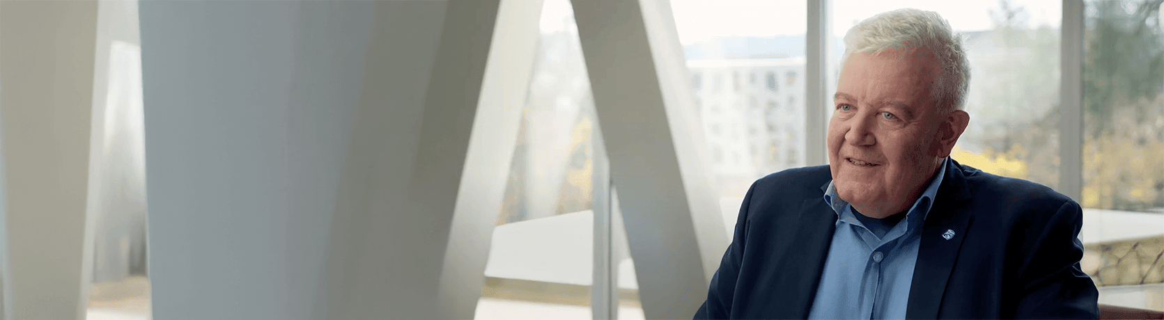 Dr. Peter Koch sits indoors near large windows with natural light and architectural features.