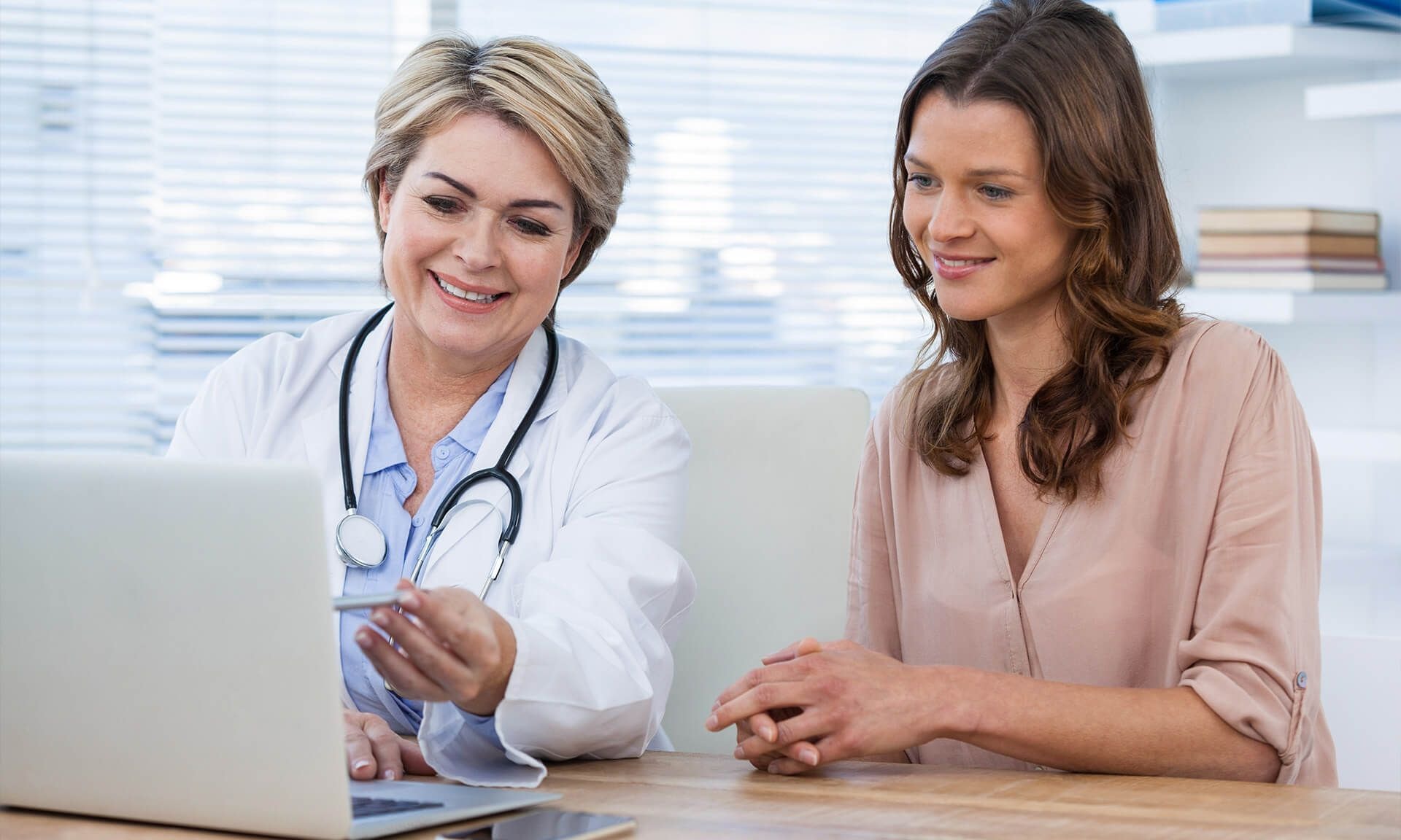 A female doctor and a female patient looking at a laptop screen in an office environment.