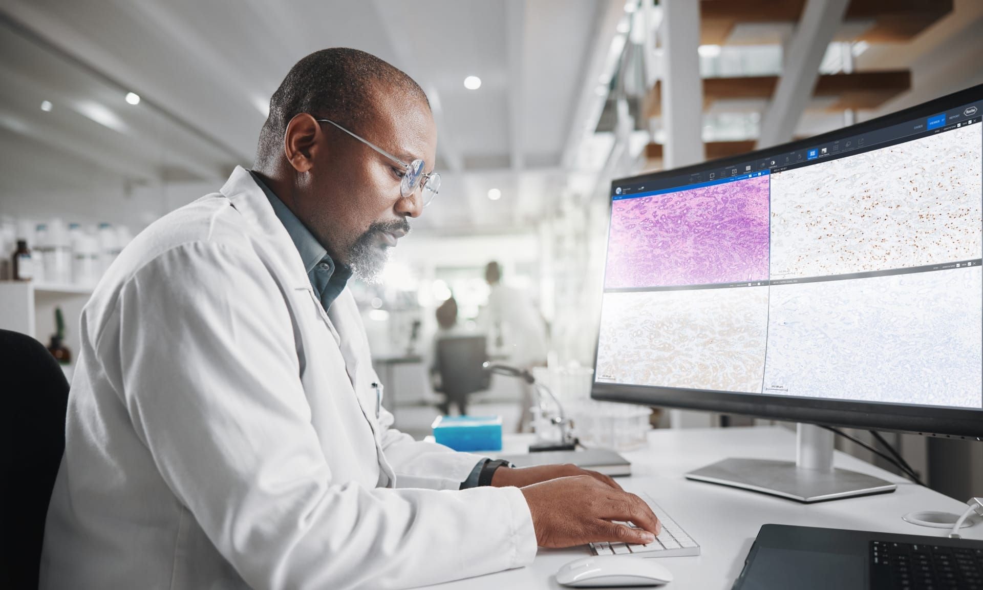 A male doctor working at his desk in front of a computer screen displaying multi-slide canvas.