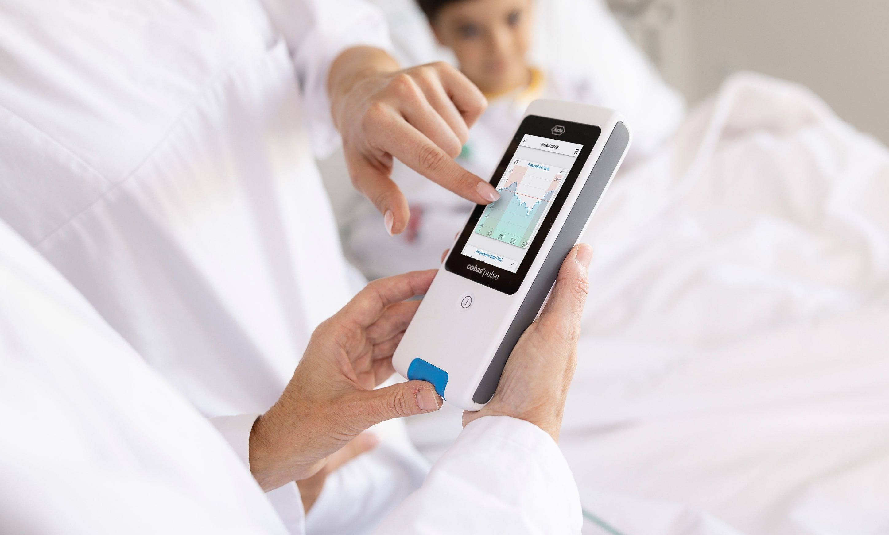 A medical professional demonstrates patient data on a handheld device in a clinical setting.