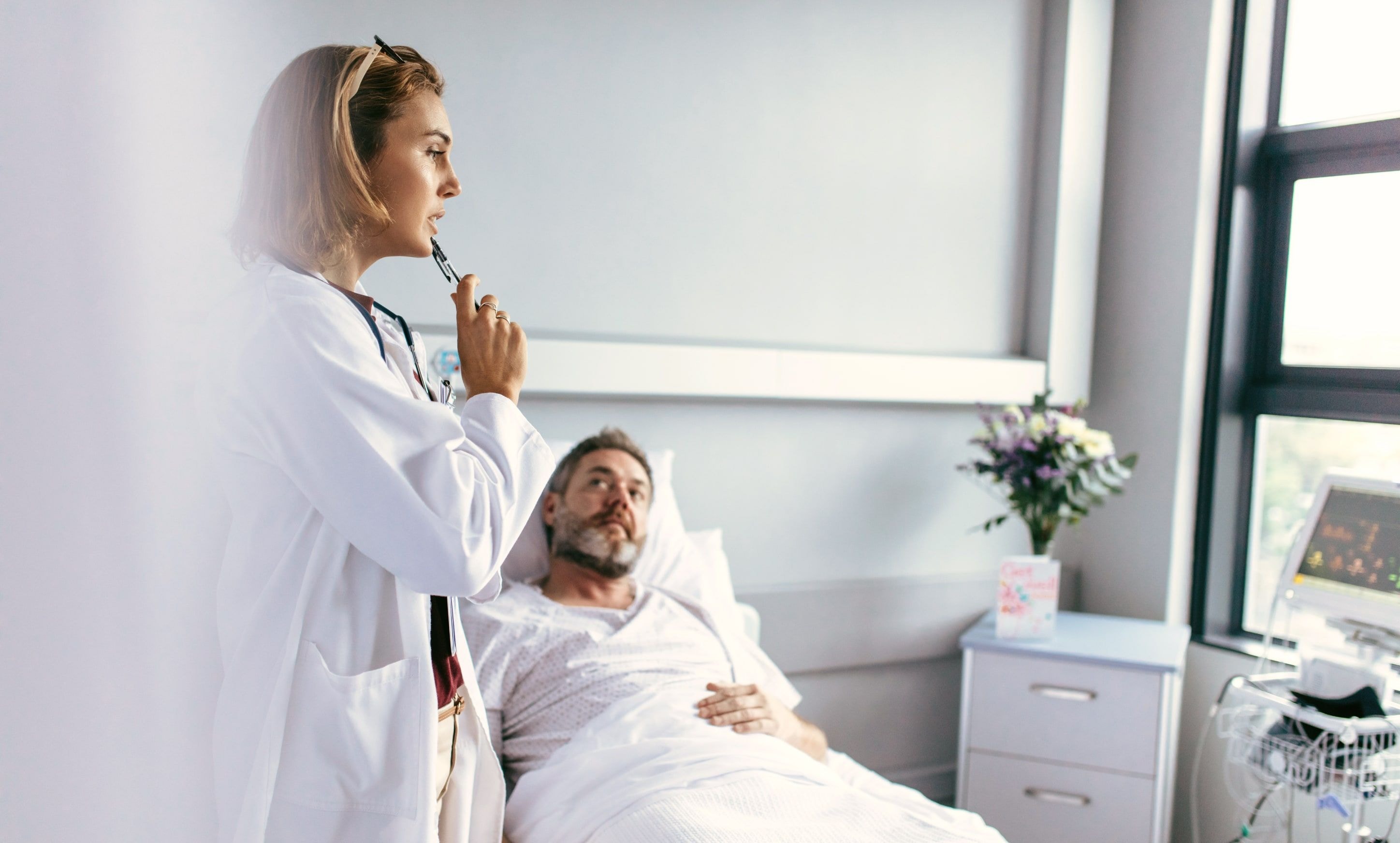 A doctor standing beside a patient lying in a hospital bed, with medical equipment in the background.