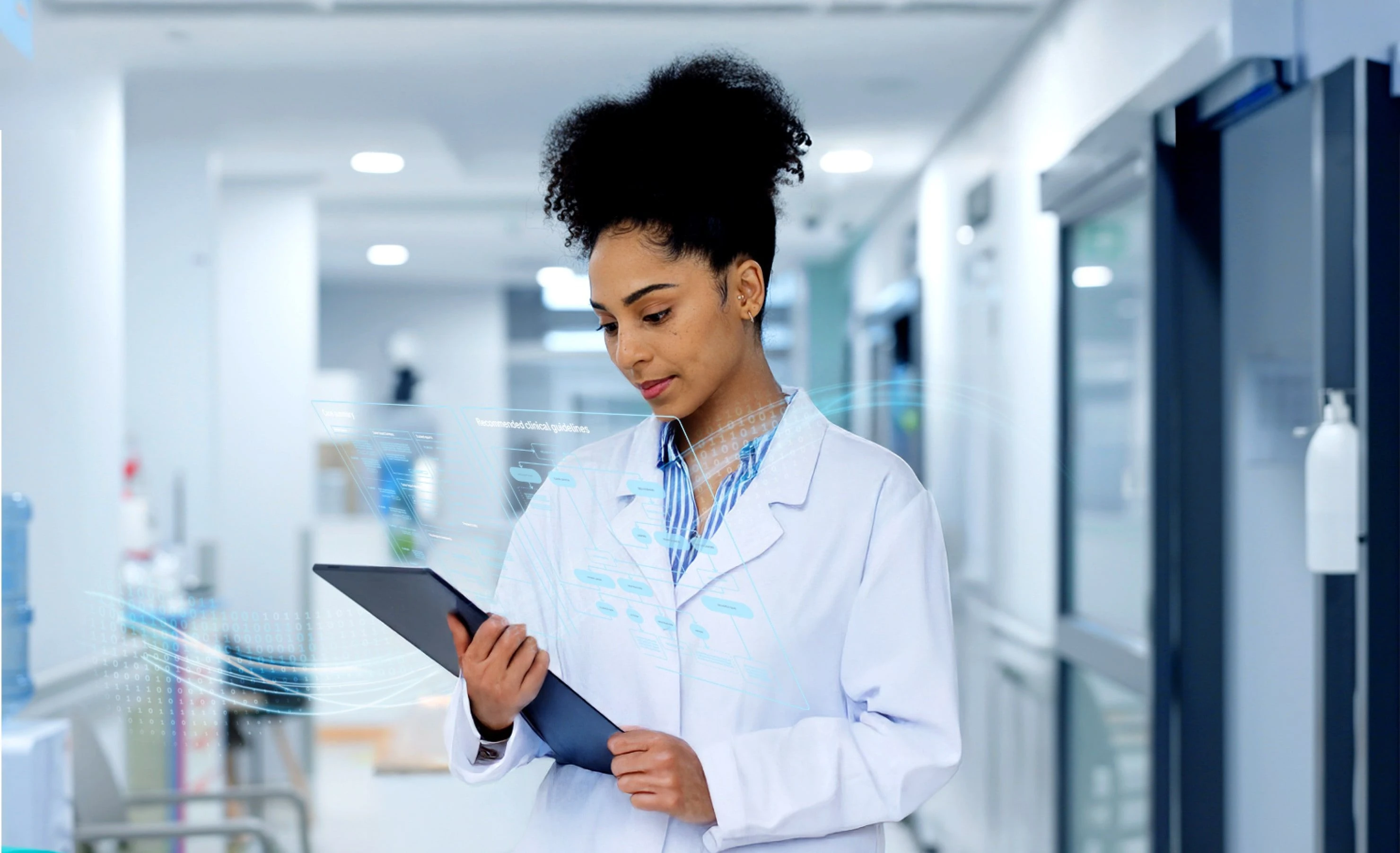 A healthcare professional reviews data on a tablet while standing in a hospital hallway.