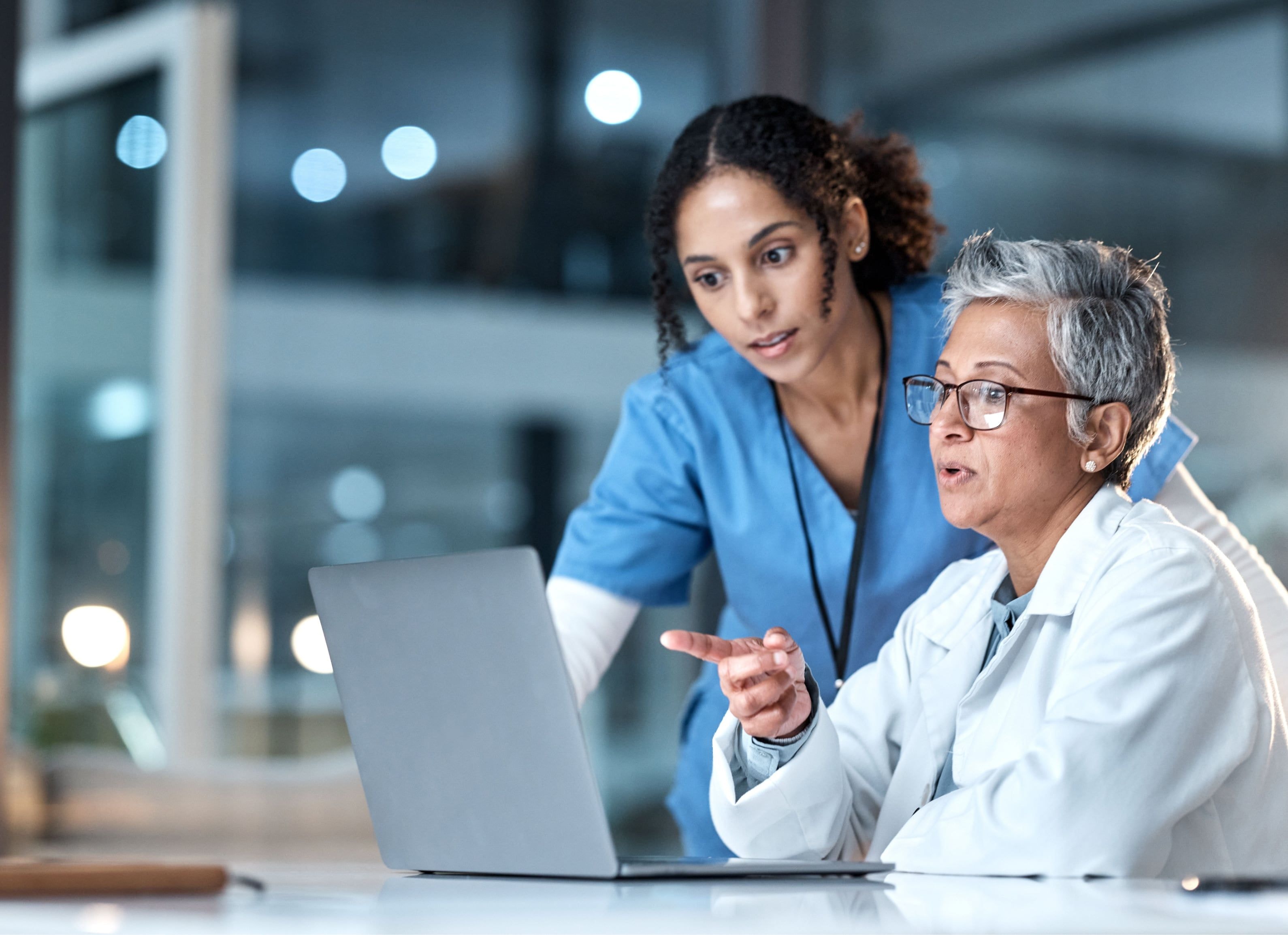 Two female doctors review medical data on a laptop.
