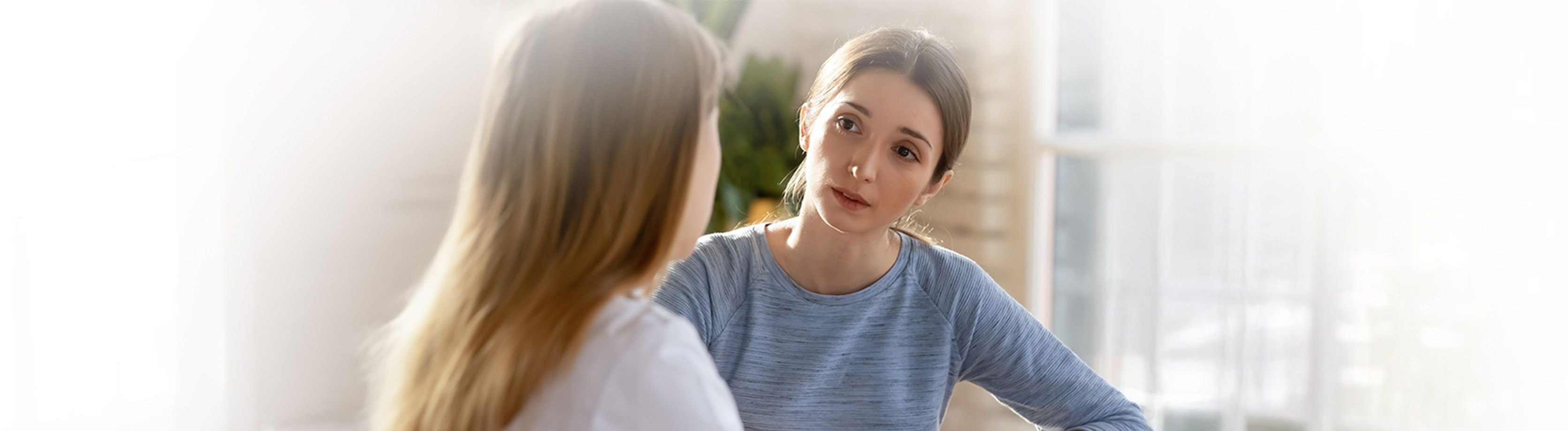 Due donne sedute in casa, impegnate in una conversazione seria. Una donna ascolta attentamente, mentre l'altra sembra parlare.