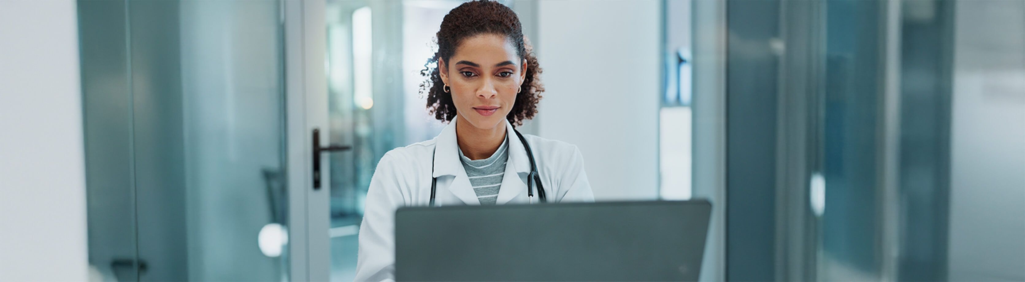 A medical professional reviewing patient data on her laptop in a bright, clinical environment.