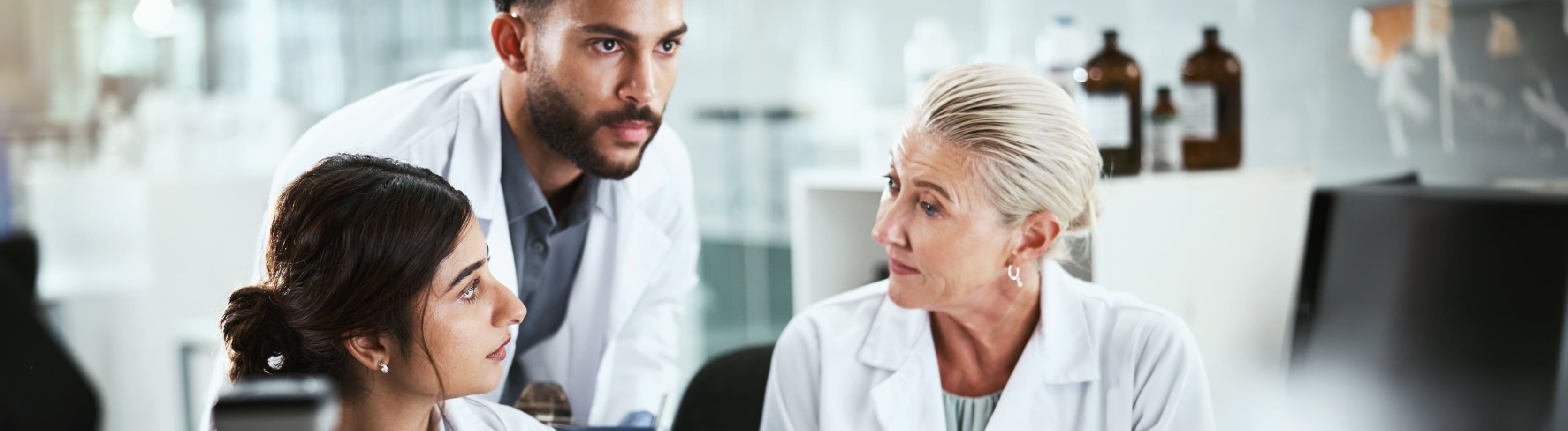 A diverse group of three healthcare professionals in lab coats engaged in a serious discussion.