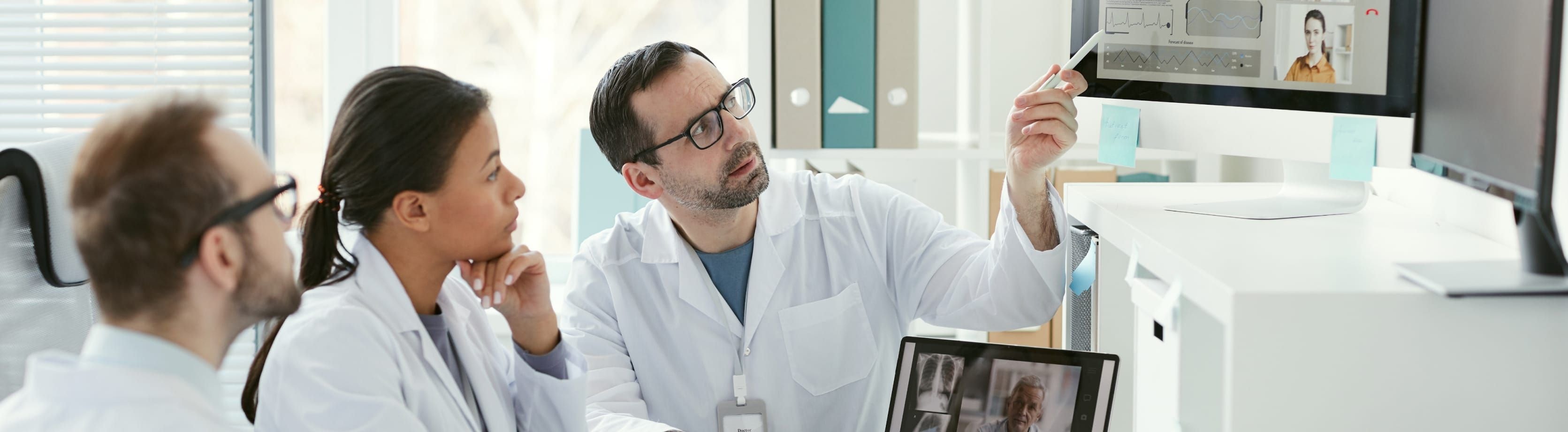 Three doctors in a meeting watching a screen on the wall.
