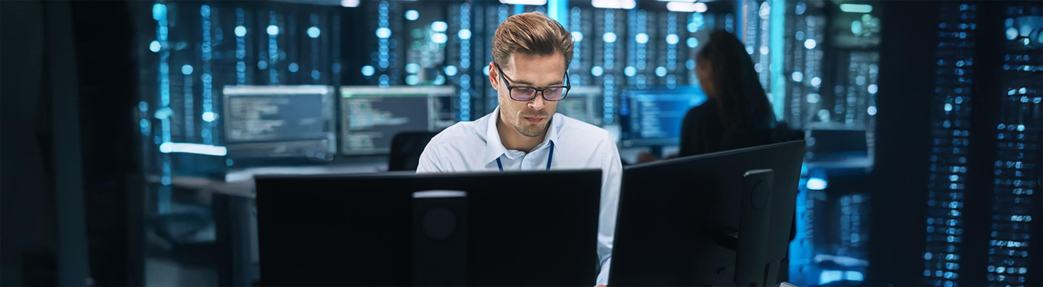 Male IT professional working at a computer, monitoring cybersecurity systems in a secure server room environment.