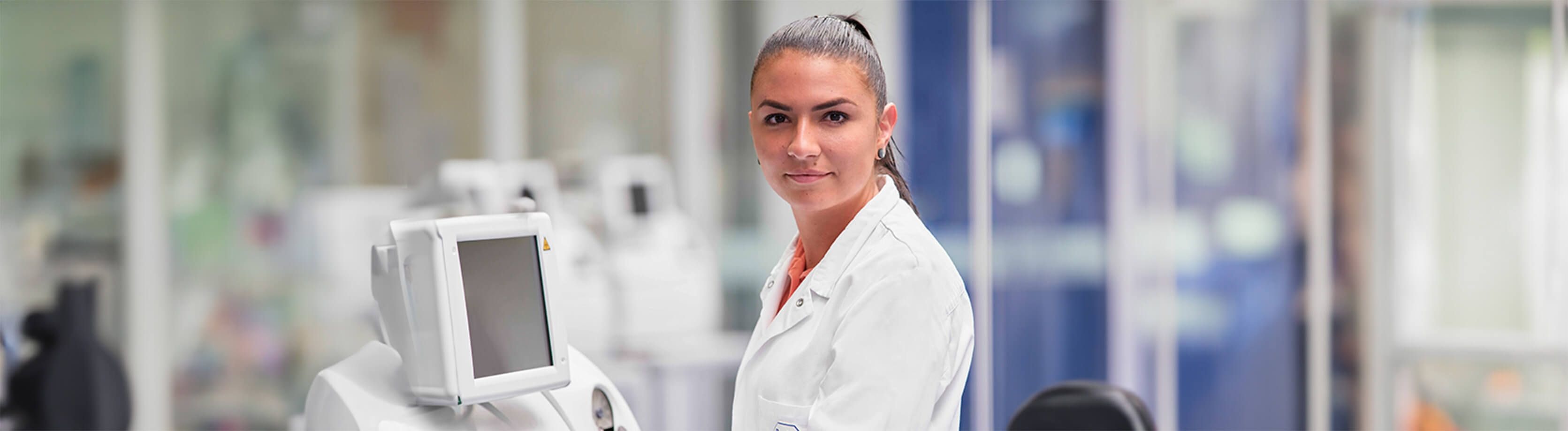 Female lab professional standing by a lab instrument screen.