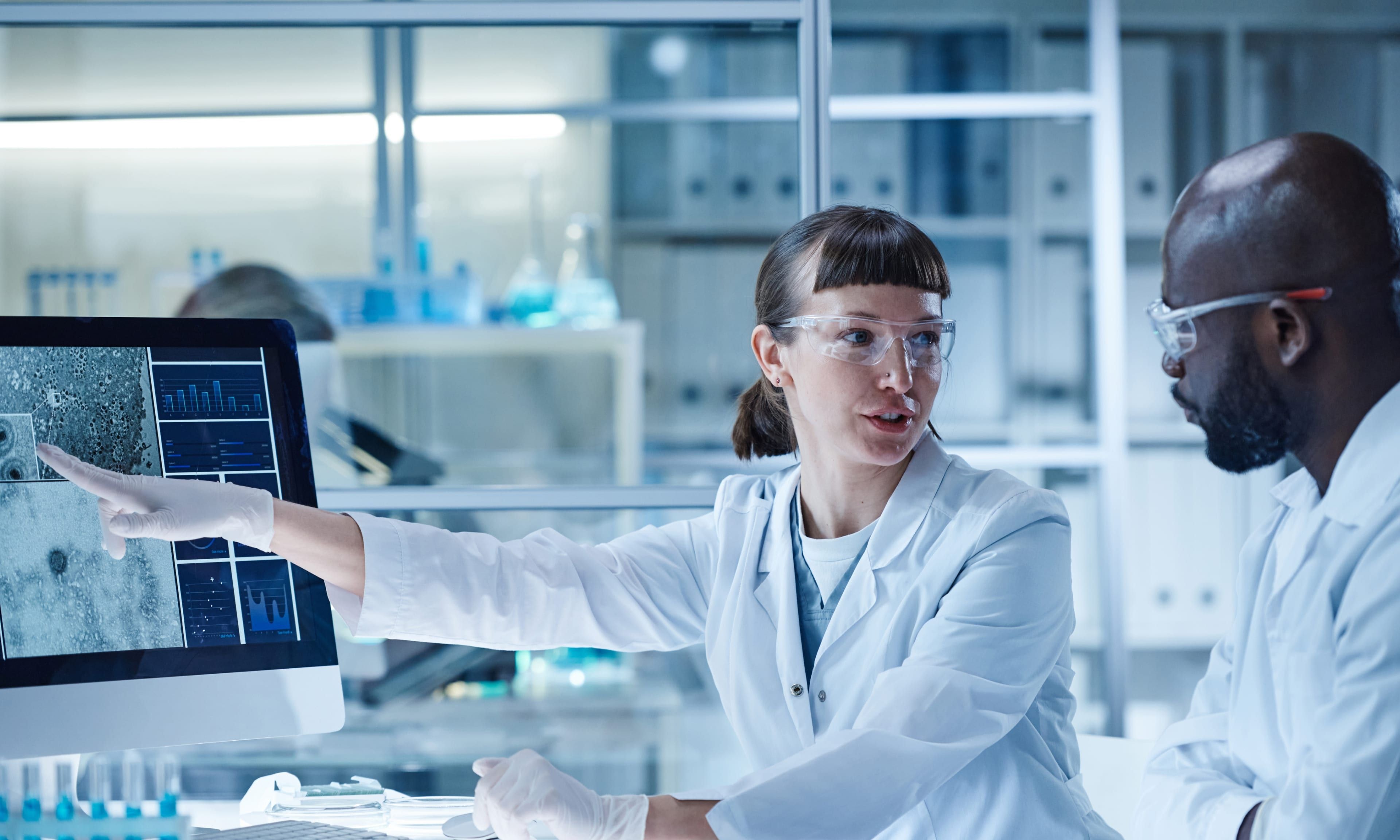 Two lab technicians working by a computer screen in a laboratory environment.