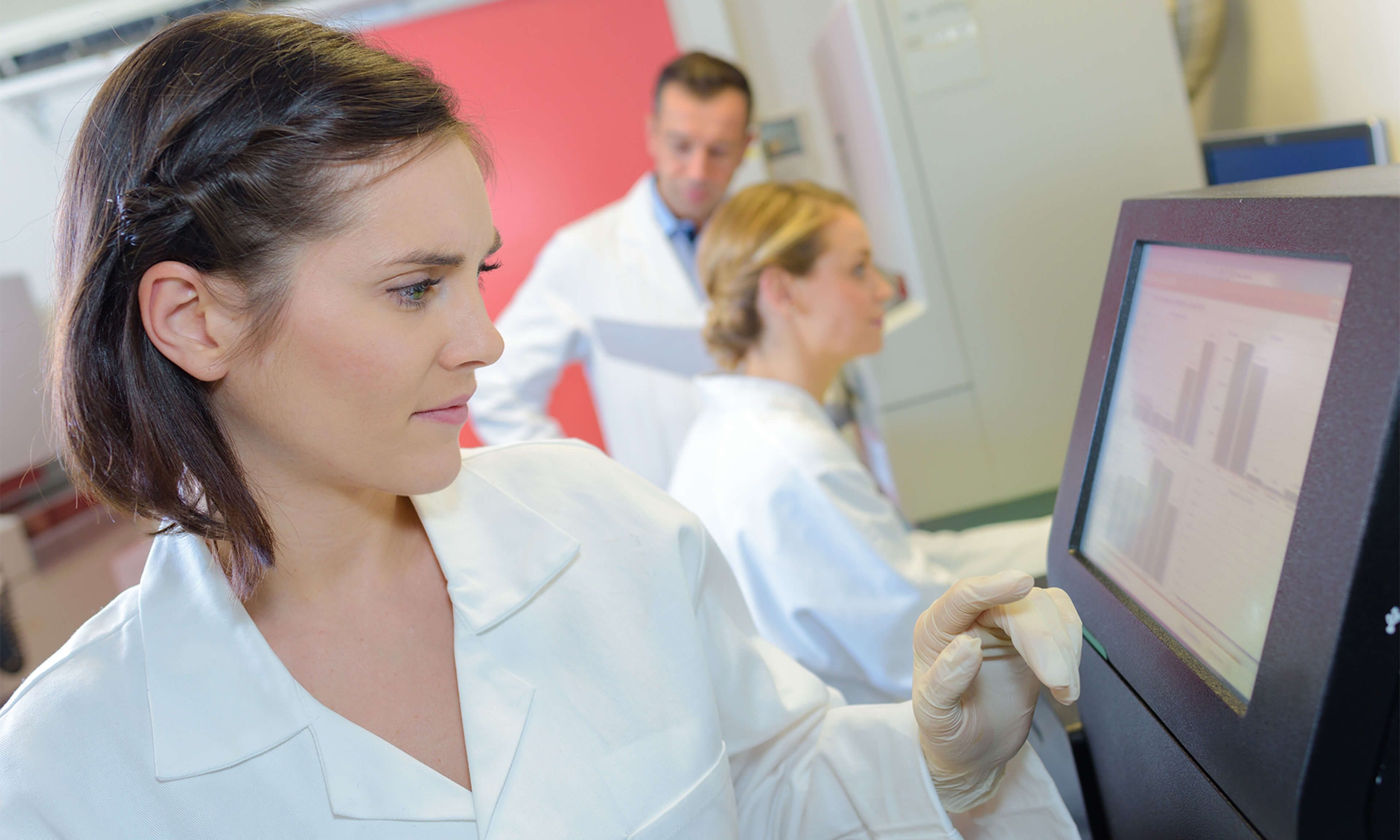 Scientist interacting with a touchscreen monitor in a clinical laboratory setting, focusing on data analysis and lab workflows.