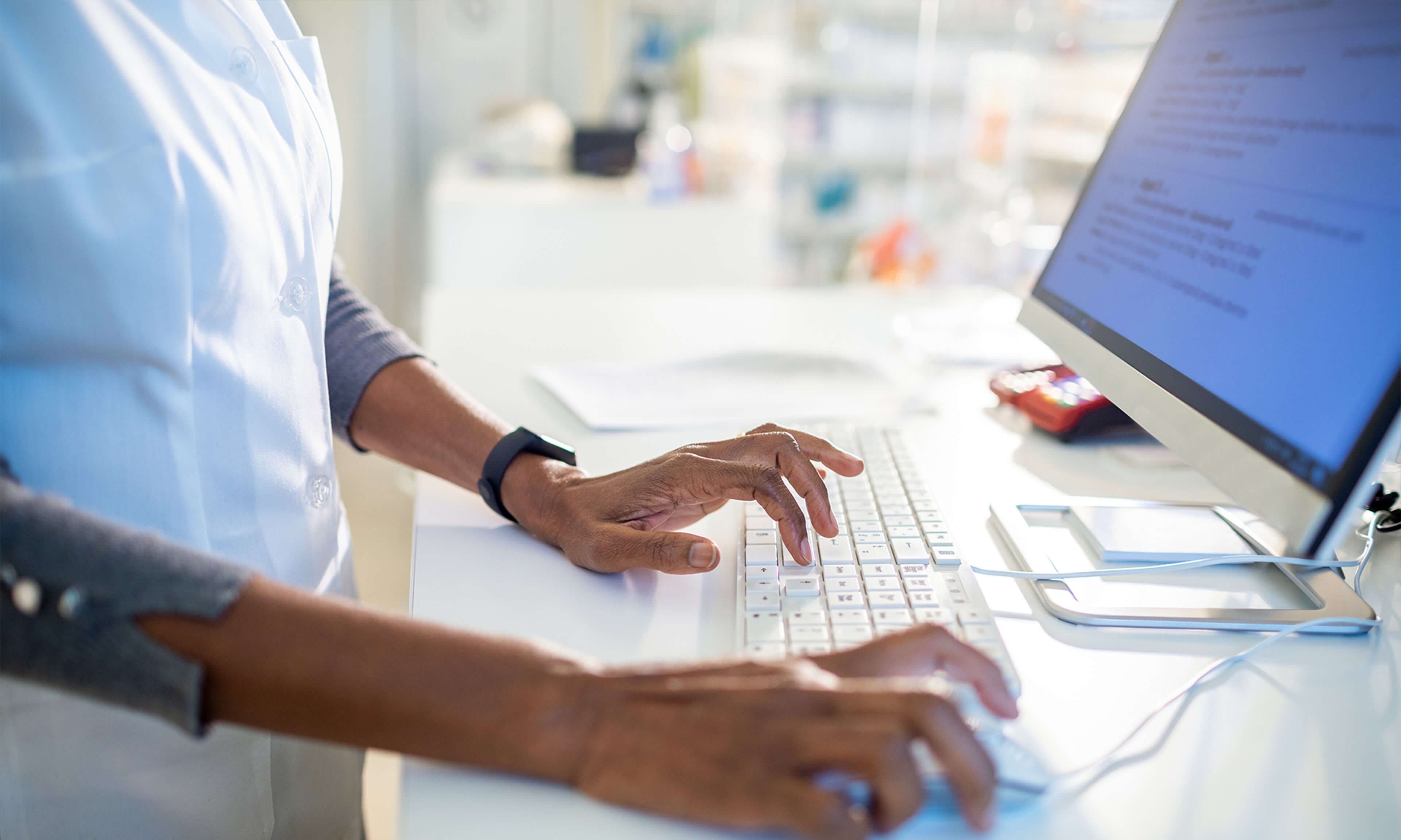 Operatore sanitario che digita su un computer desktop in un ambiente di laboratorio pulito, a rappresentare una gestione accurata dei dati in ambito medico.