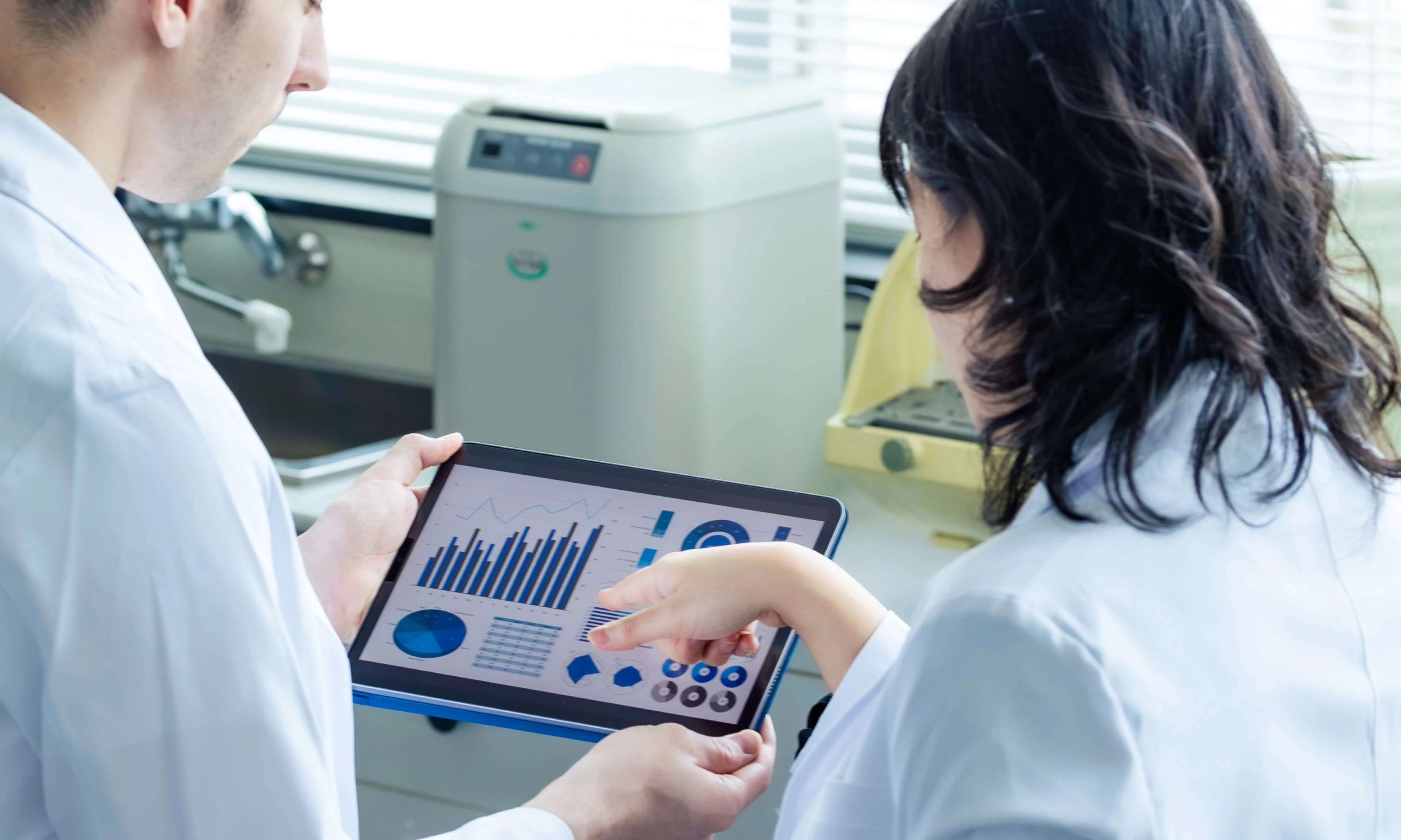 Two lab technicians studying a dashboard on a tablet device.