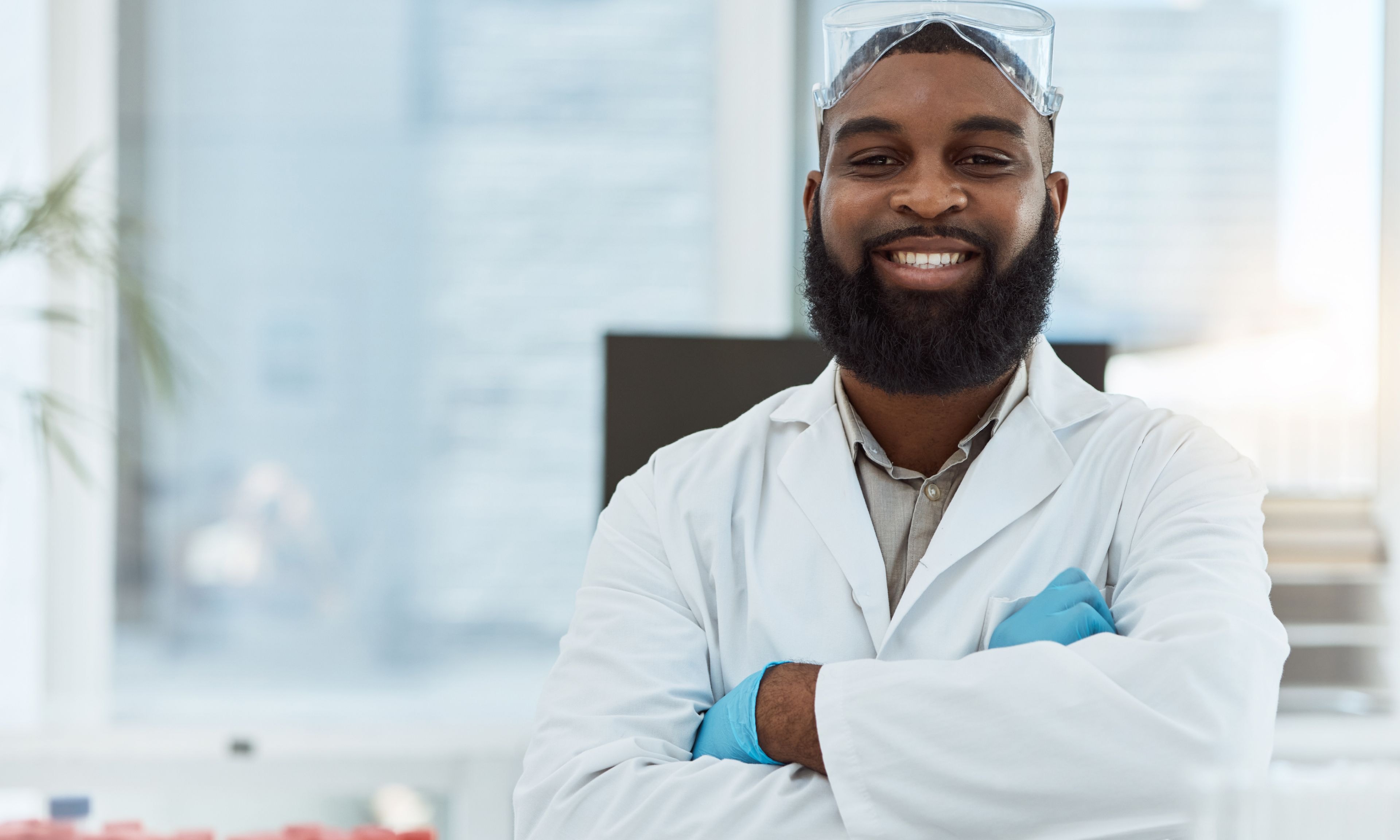 A confident scientist stands with folded arms in a bright laboratory setting.
