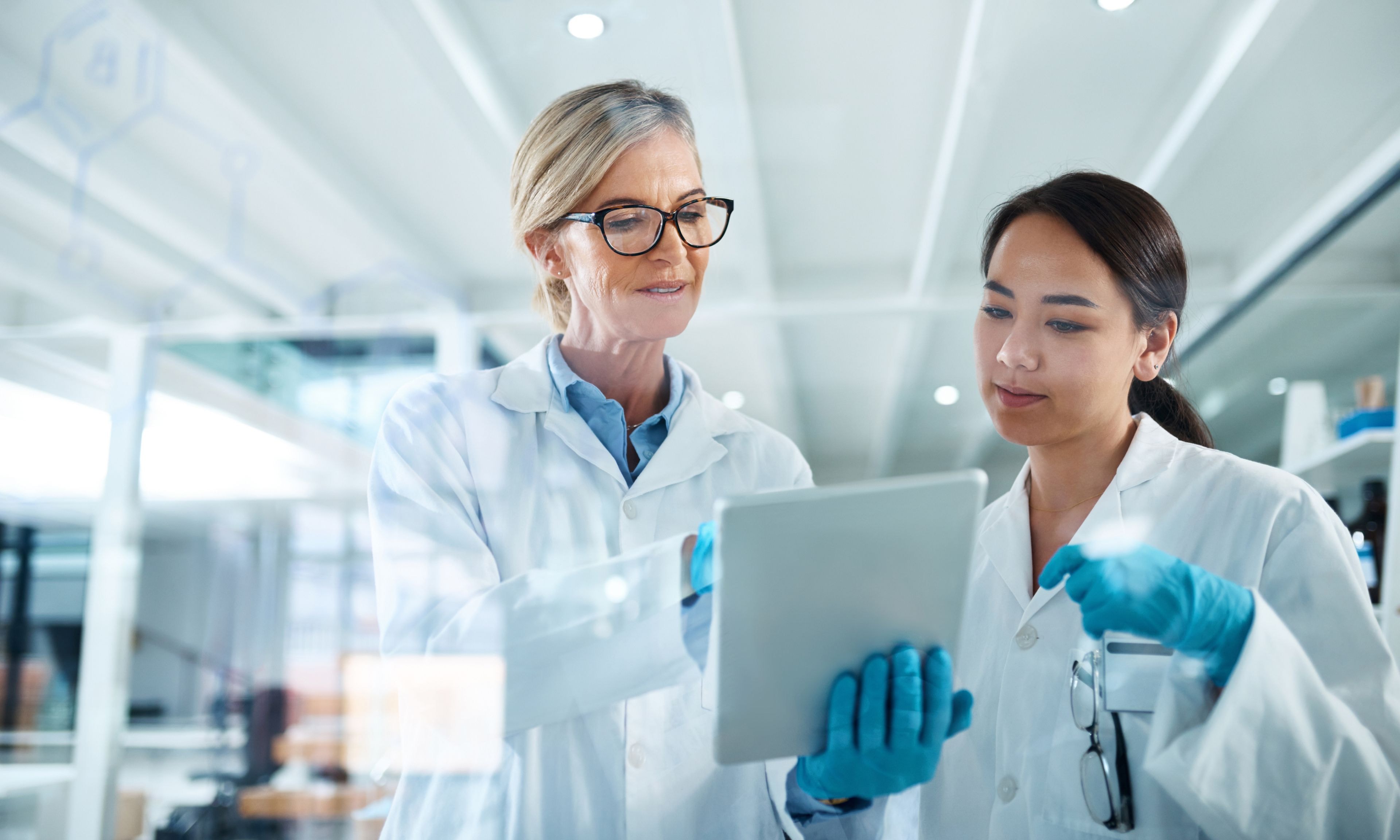 Two researchers in lab coats discuss data displayed on a tablet in a bright laboratory.