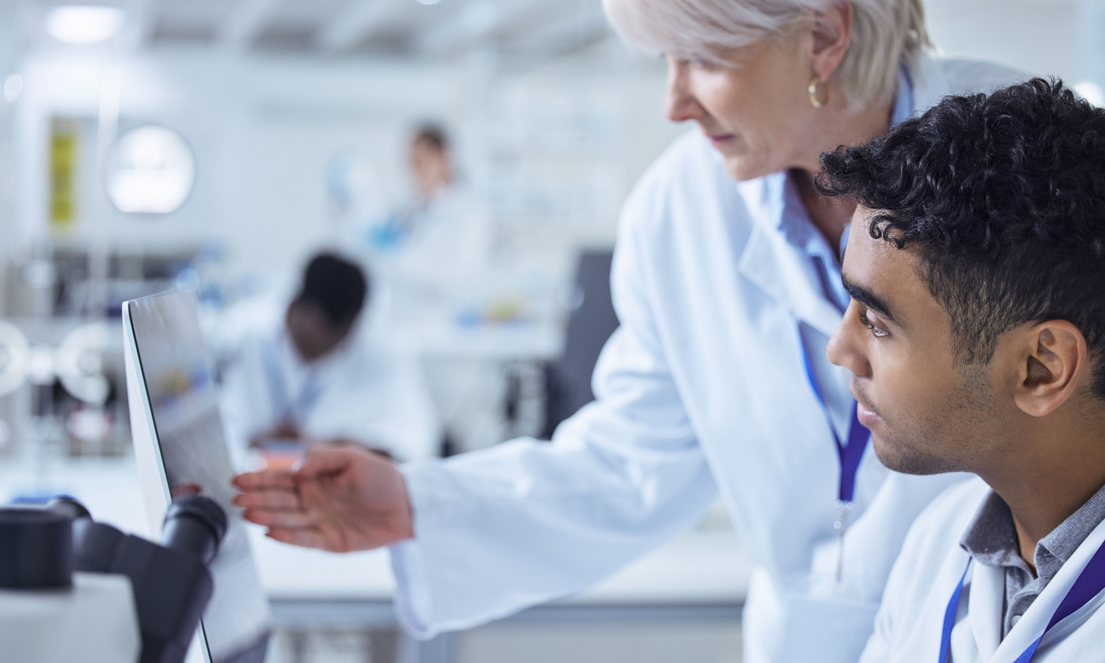 Researchers in a laboratory analyze data on a computer screen while discussing their findings.
