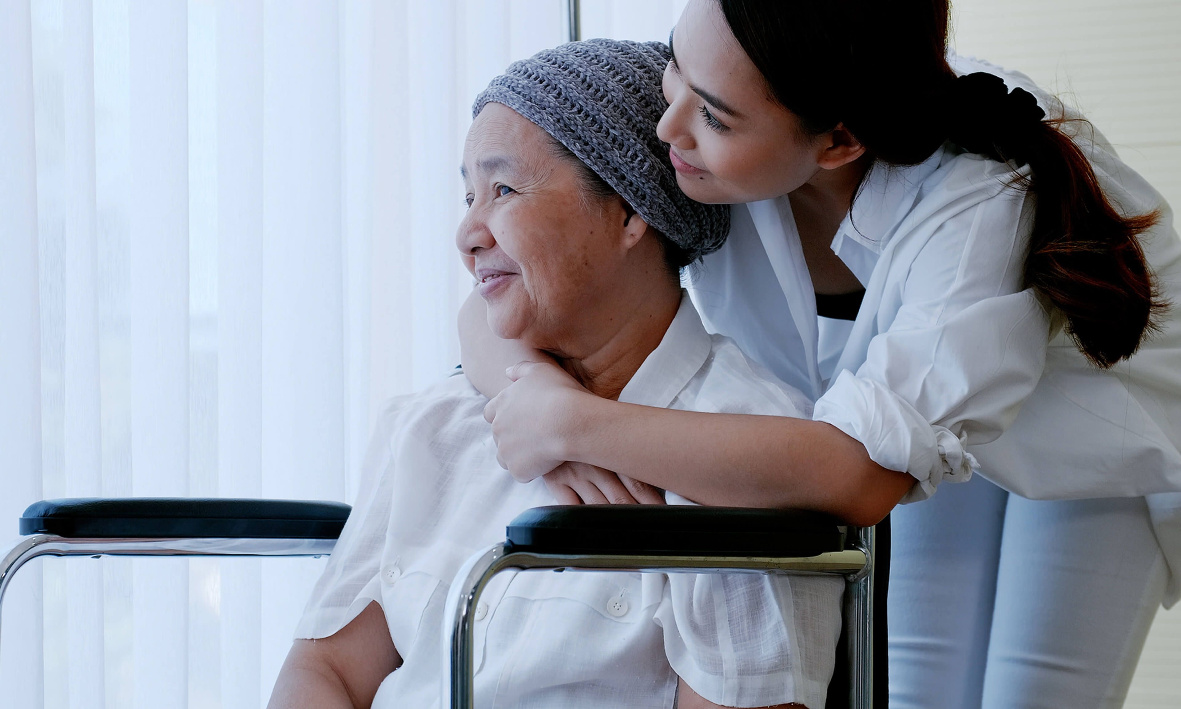 A caregiver embracing a patient in a wheelchair, both smiling, symbolizing compassion and healthcare support.