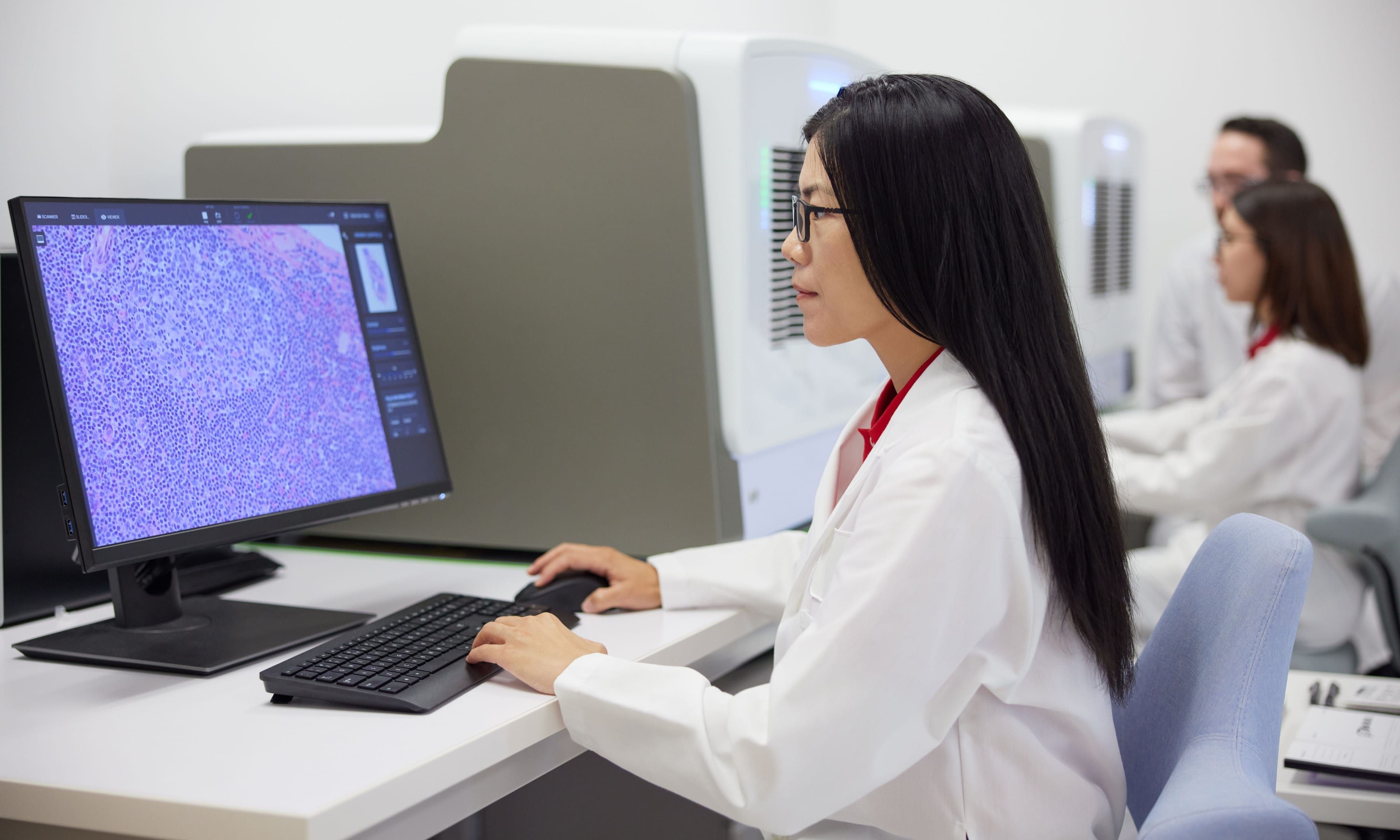 A laboratory professional analyzes medical images on a computer screen in a clinical lab.