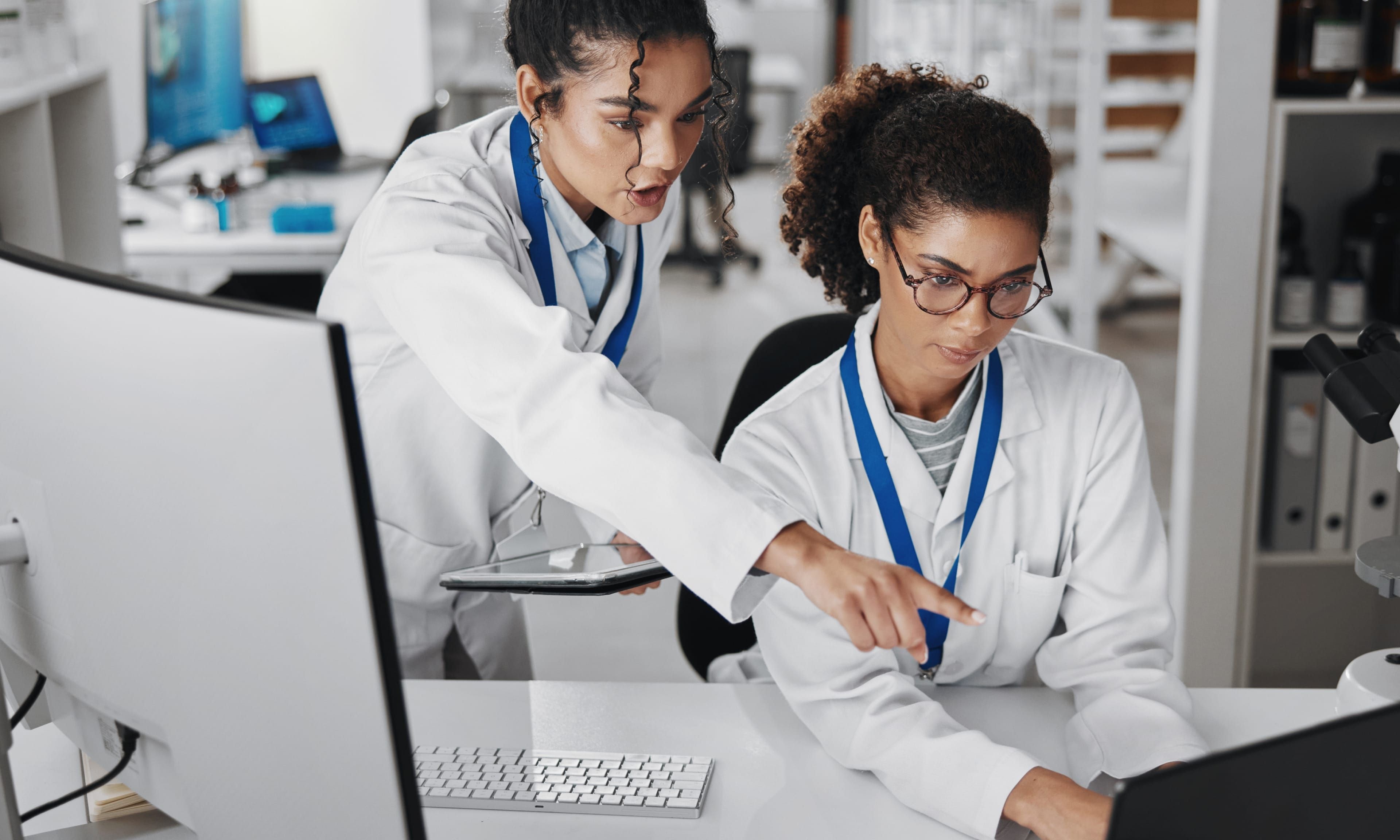 Two medical professionals in lab coats discuss information displayed on a computer screen.