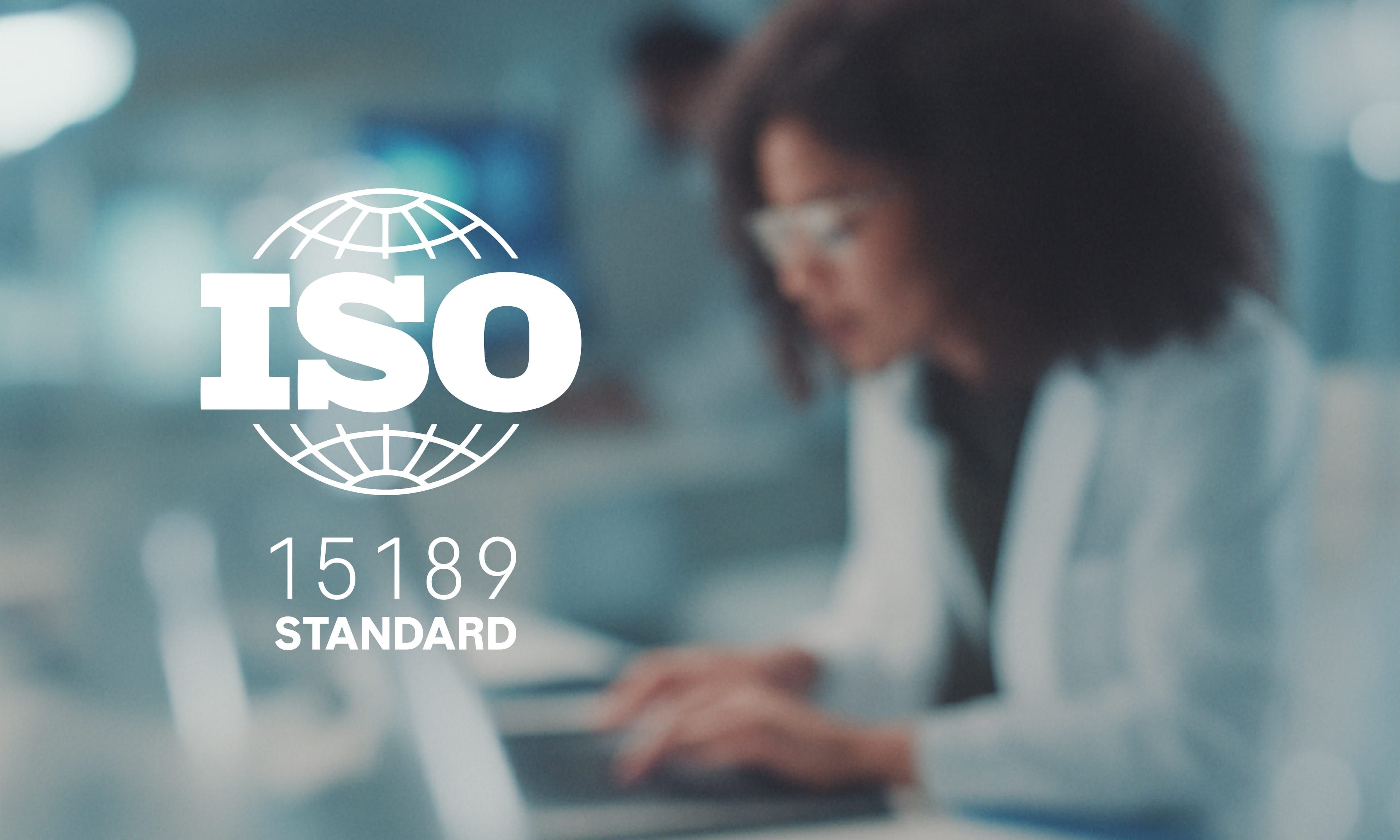 Laboratory professional working at a desk with ISO 15189 standard prominently displayed.