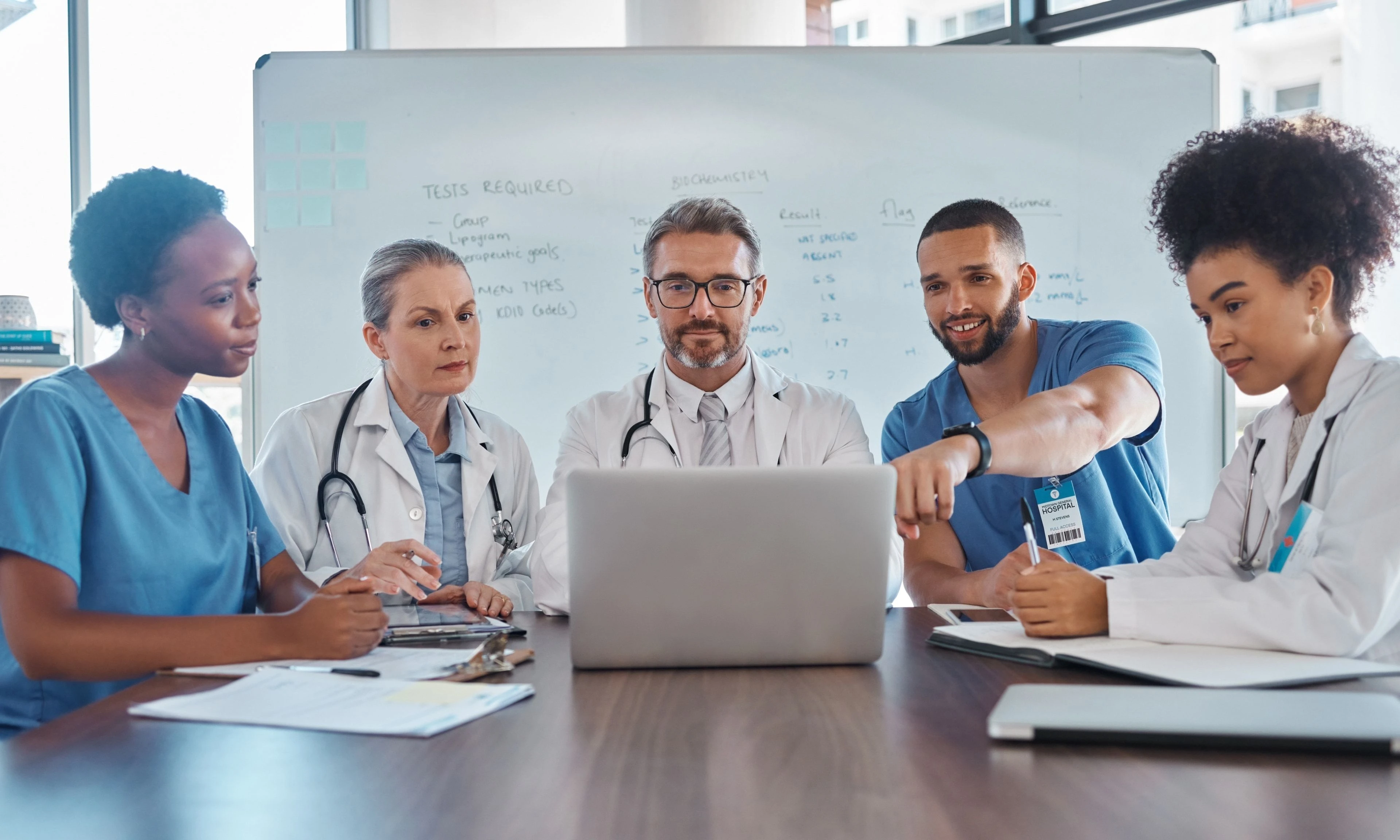 A diverse team of medical professionals in a meeting, discussing content displayed on a laptop in a conference room.