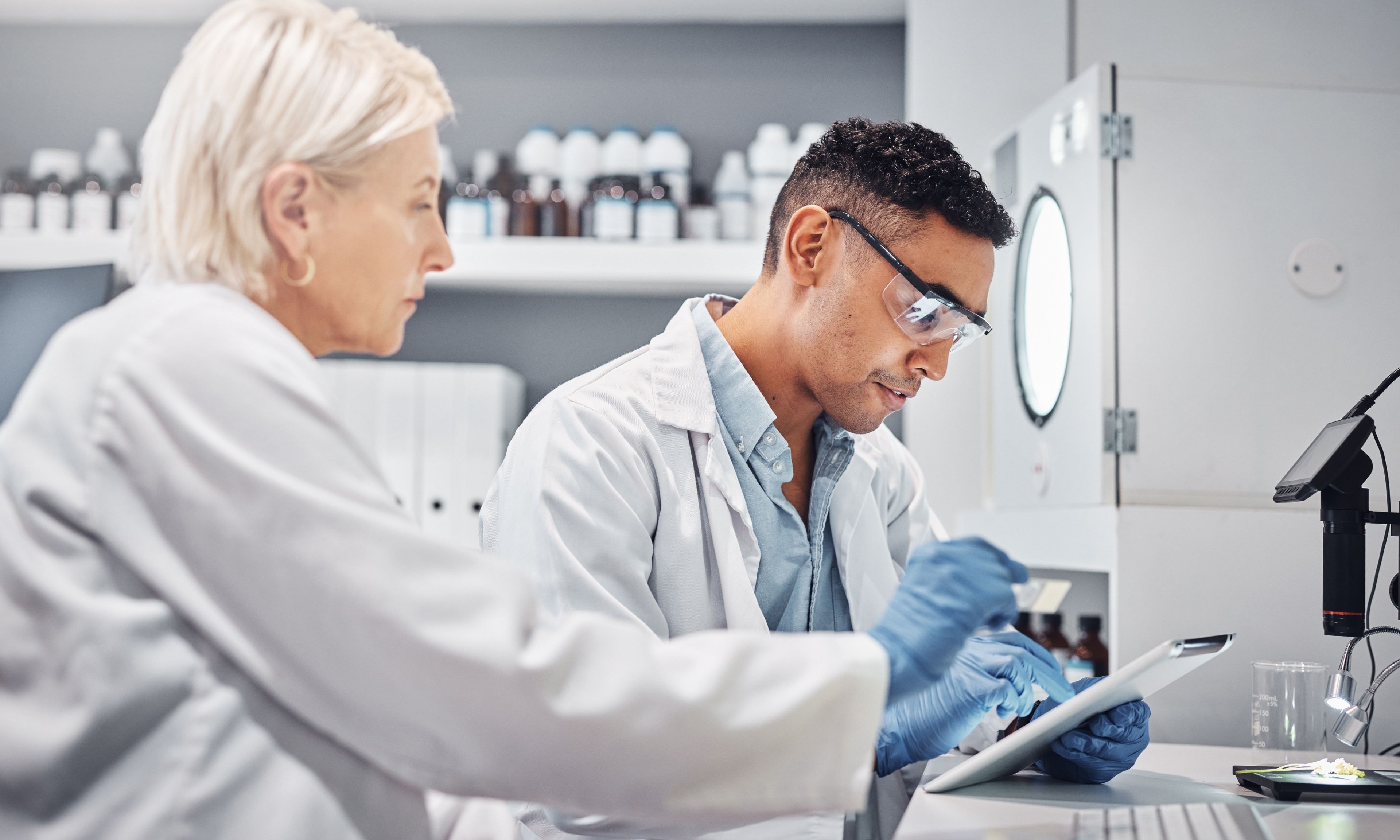 Two laboratory colleagues review experiment results on a tablet in a research setting.
