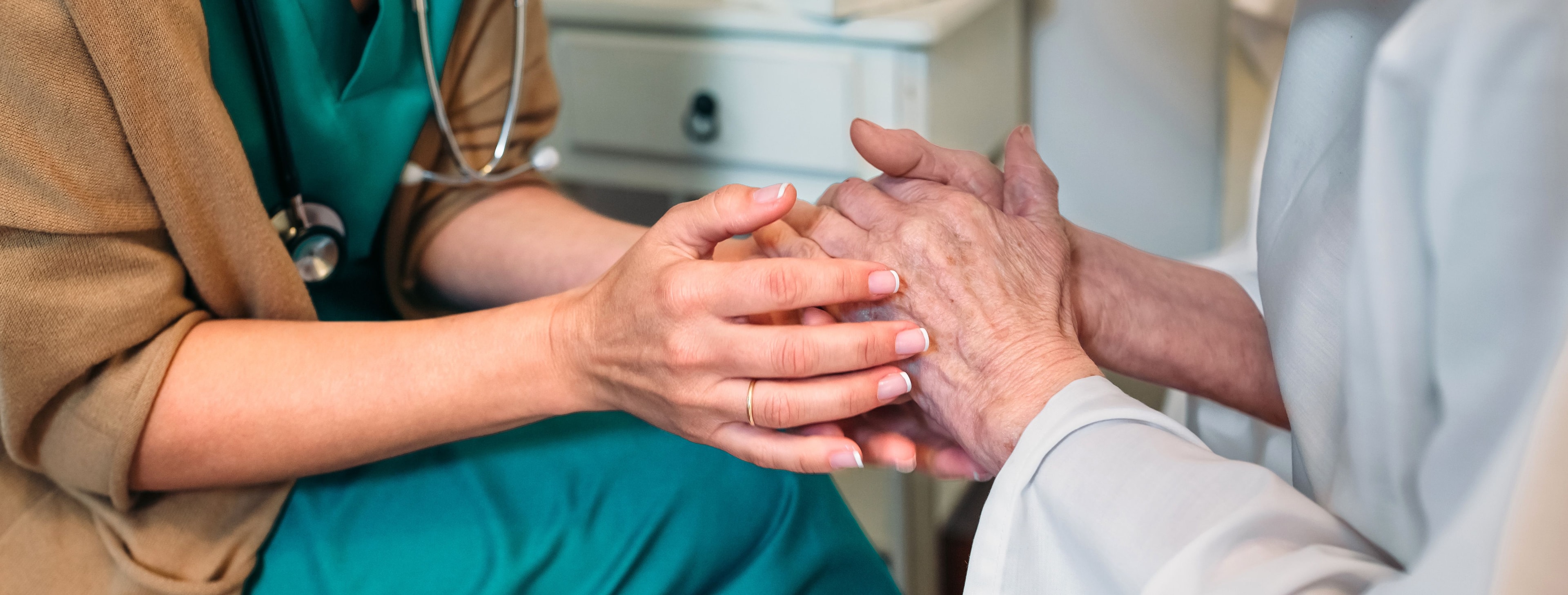A caregiver gently holds an elderly patient's hands, providing comfort and support.