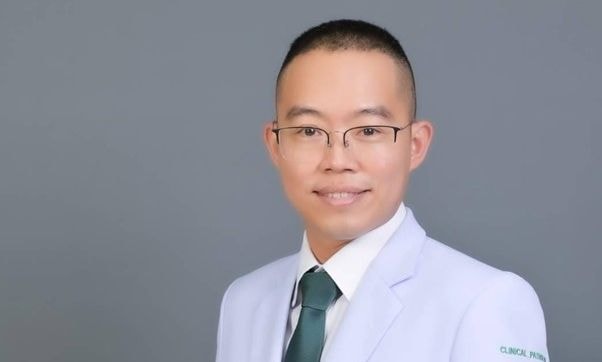 Col. Pitipat Jamnarnwej in a white clinical uniform with a green tie, posing against a gray background.