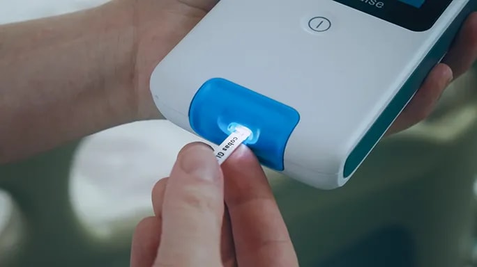 A close-up of a cobas® pulse device with a blood glucose test strip inserted, part of the GlucoTab® system for automated insulin dosing.