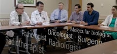 Still image featuring specialists at a multidisciplinary tumor board meeting